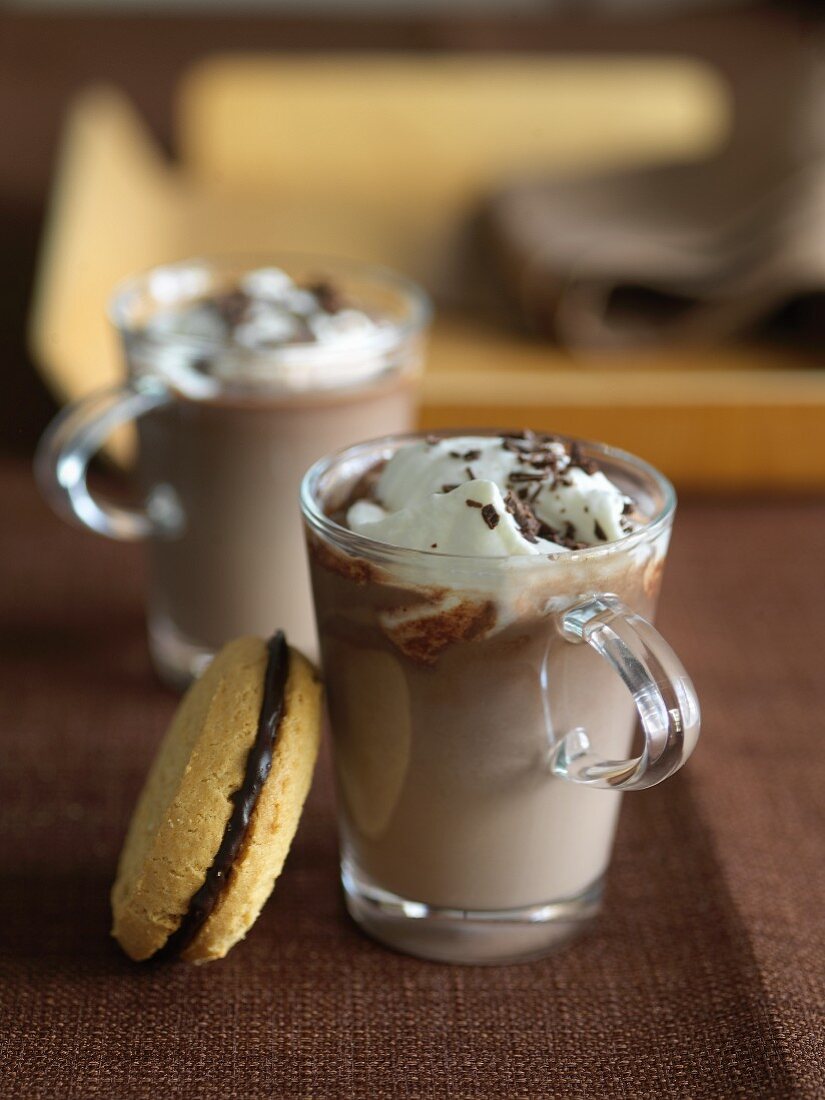 Zwei Tassen heiße Schokolade mit Sahne, Sandwich Cookies mit Schokofüllung