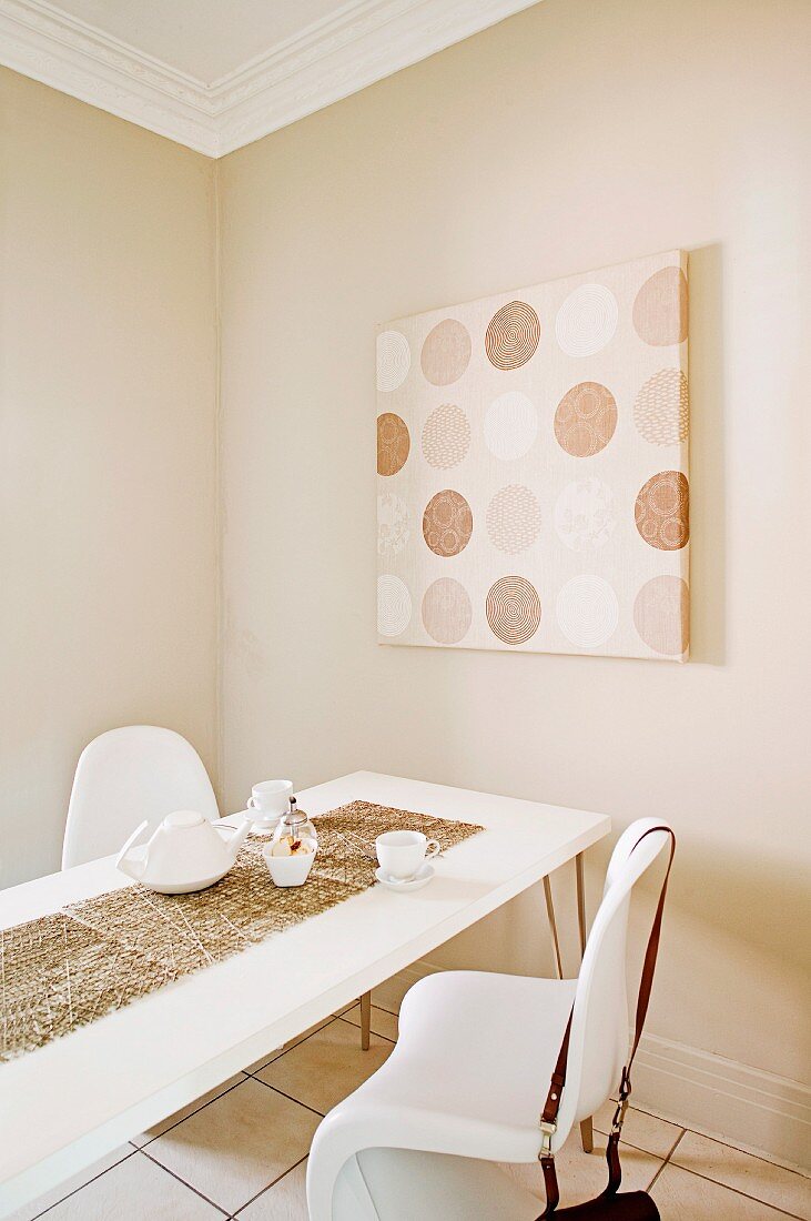 Dining table and white shell chairs in front of modern artwork on beige-painted wall