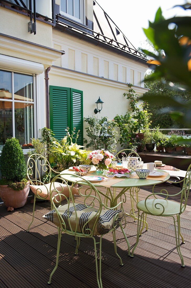 Filigrane Metall Stühle am gedeckten Nachmittagstisch auf Holzterrasse vor traditioneller Villa