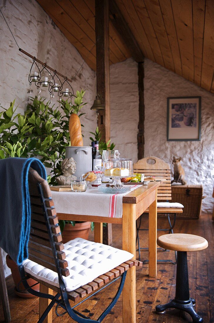 Rustic conservatory with sloping, wooden ceiling and wooden columns; set wooden table and garden chair with seat cushion in foreground