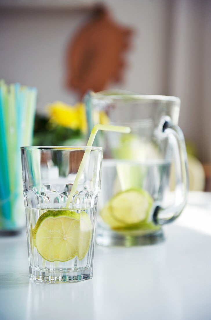 Glasses and jug of lemon water on white table