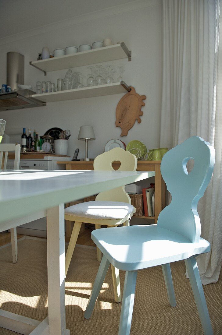 Pastel farmhouse chairs around white-painted dining table in bright, simple kitchen