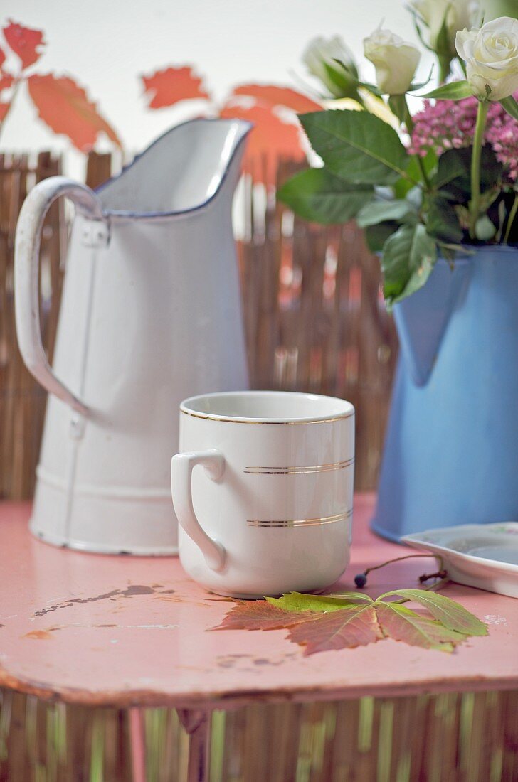 Tasse mit Goldrand und zwei alte Emaillekannen, eine mit Blumen