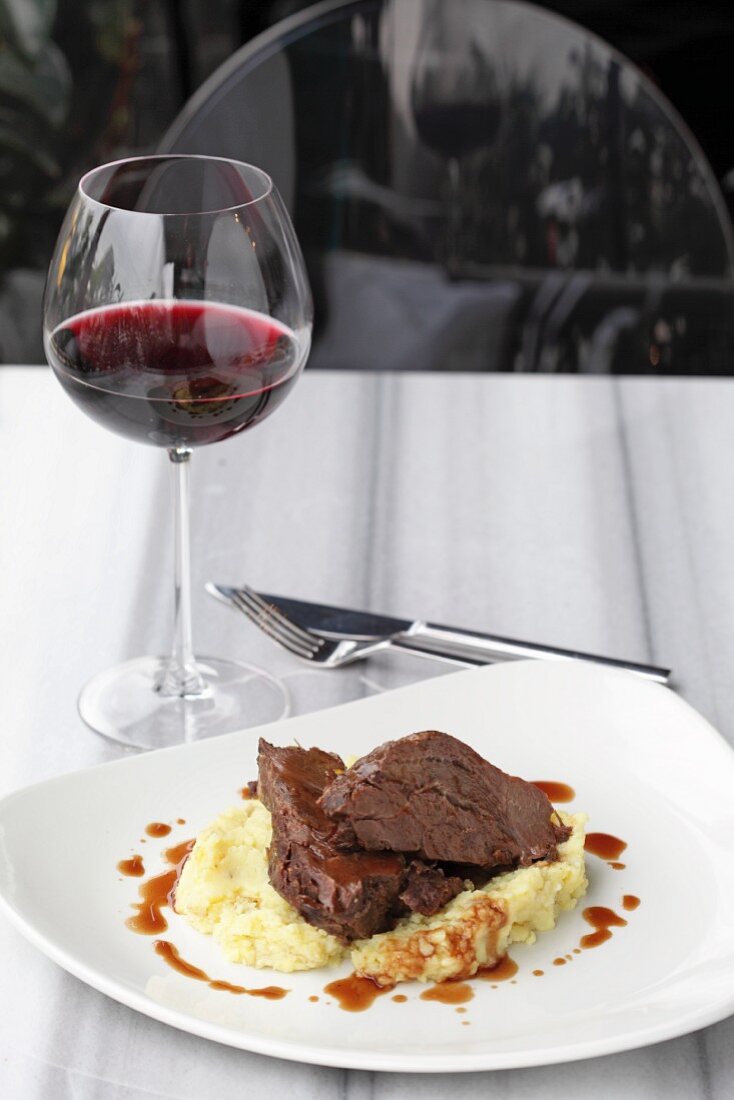 Slices of veal on mashed potato with a glass of red wine