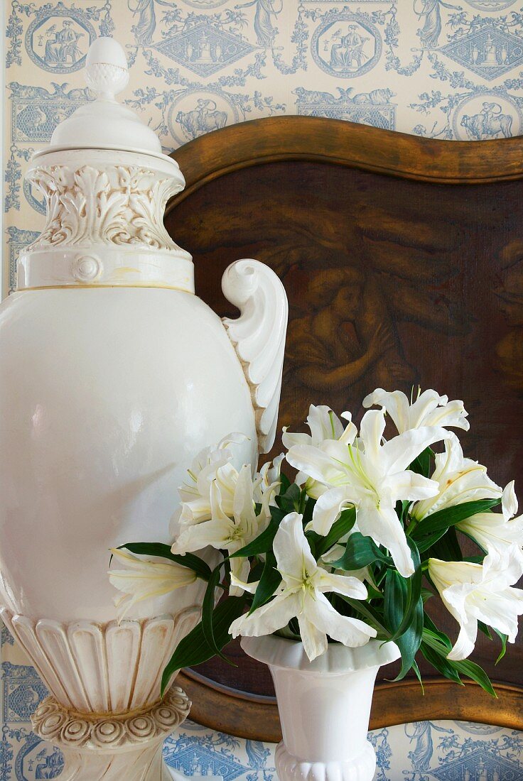 Cup-like vase and bouquet of flowers in front of image on wallpapered wall with white blue patterns