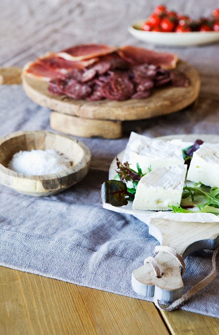 Cheeseboard, salt and cold cuts on linen tablecloth on rustic wooden table