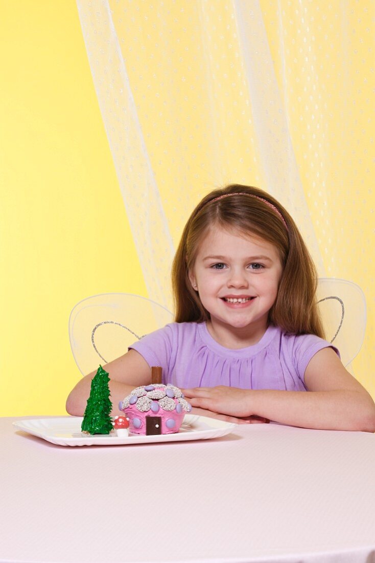Mädchen mit Engelsflügeln und Fairy House Cakes auf einem Teller