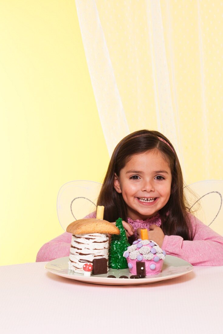 Mädchen mit Engelsflügeln und Fairy House Cakes auf einem Teller