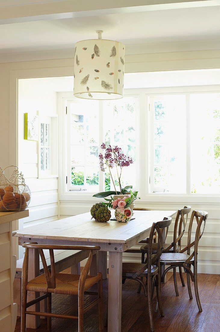 Simple wooden table and classic chairs below pendant lamp with paper lampshade in wood-panelled bay window