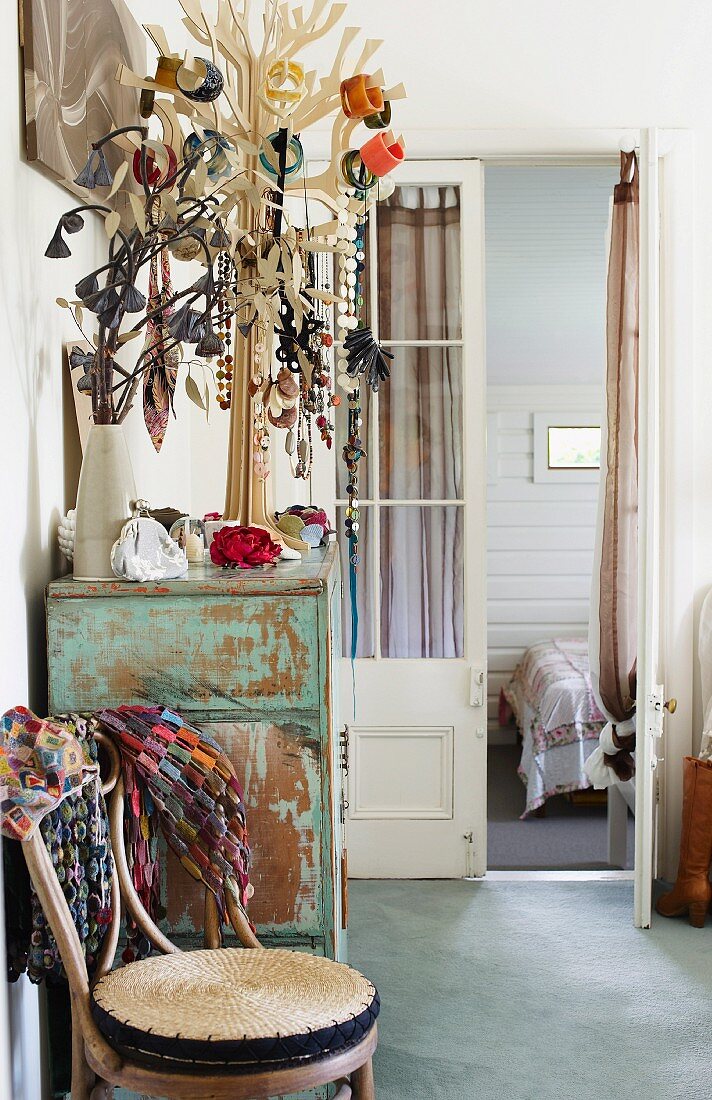 Thonet chair next to jewellery rack on vintage cabinet in front of open bedroom door