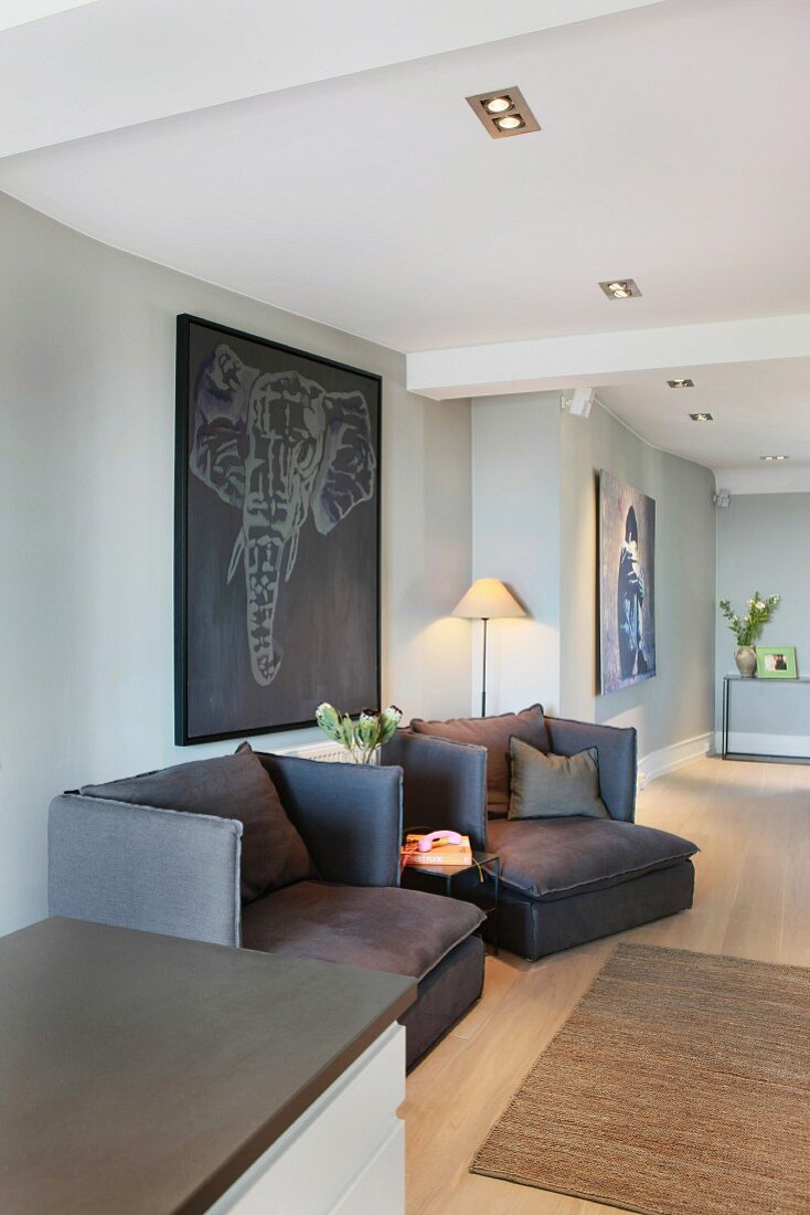 Dark armchairs below picture of elephant on grey wall in spacious, modern living room