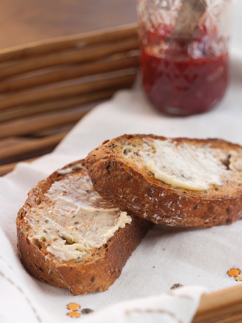 Two Pieces of Buttered Multi-Grain Toast; Jar of Jam in Background