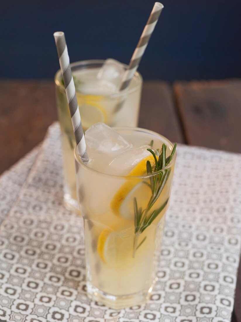 Two Glasses of Lemonade with Sprigs of Rosemary and Straws on a Wooden Table
