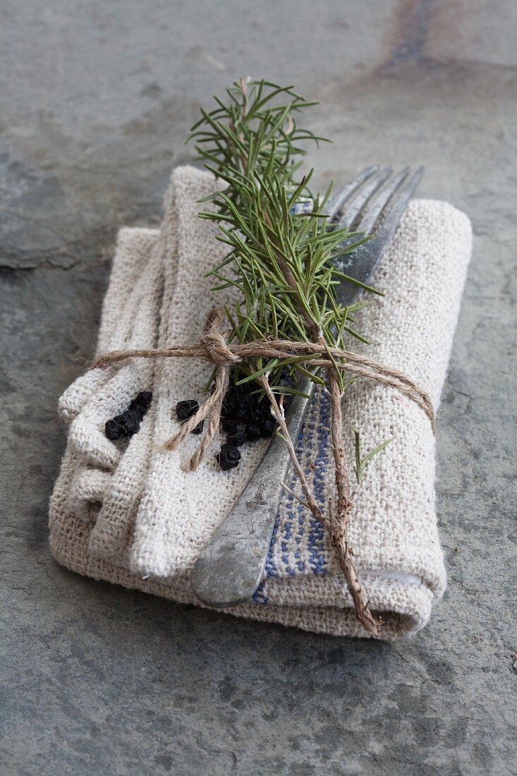 A napkin with a sprig of rosemary, dried blueberries and cutlery