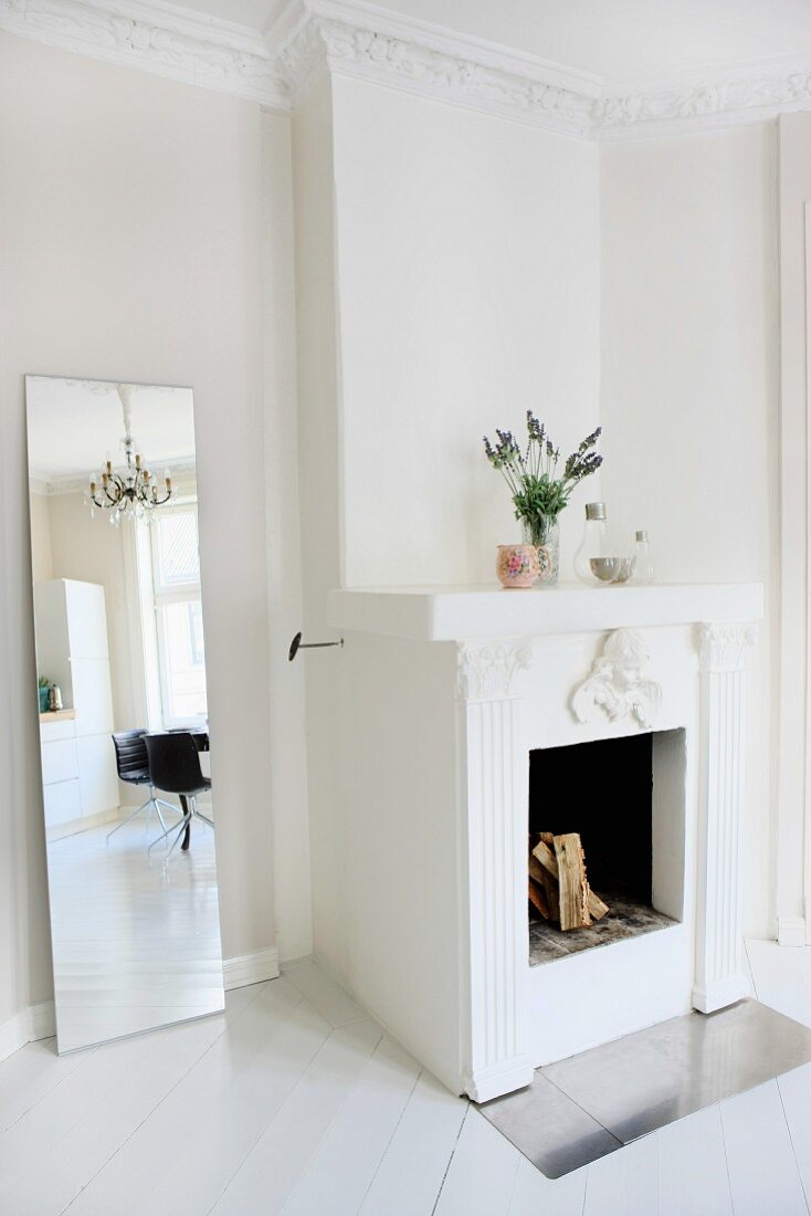 White out - modern full-length mirror next to open fireplace in renovated interior with stucco frieze