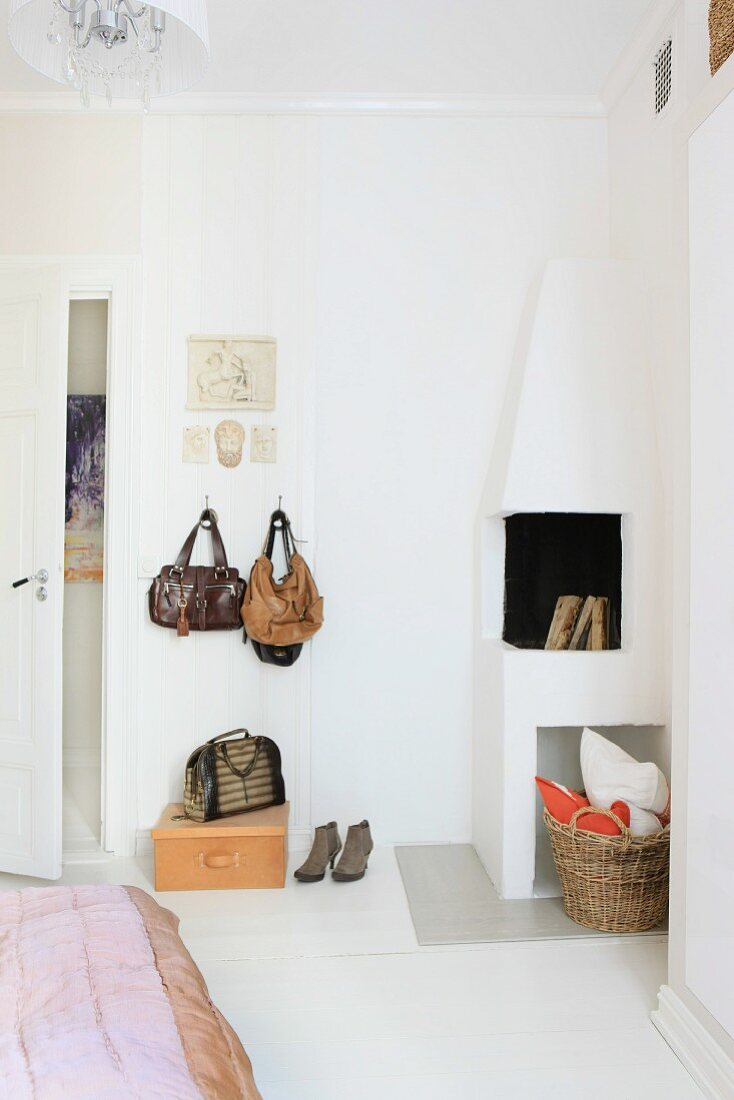Handbags hanging on wall hooks next to open corner fireplace in bedroom
