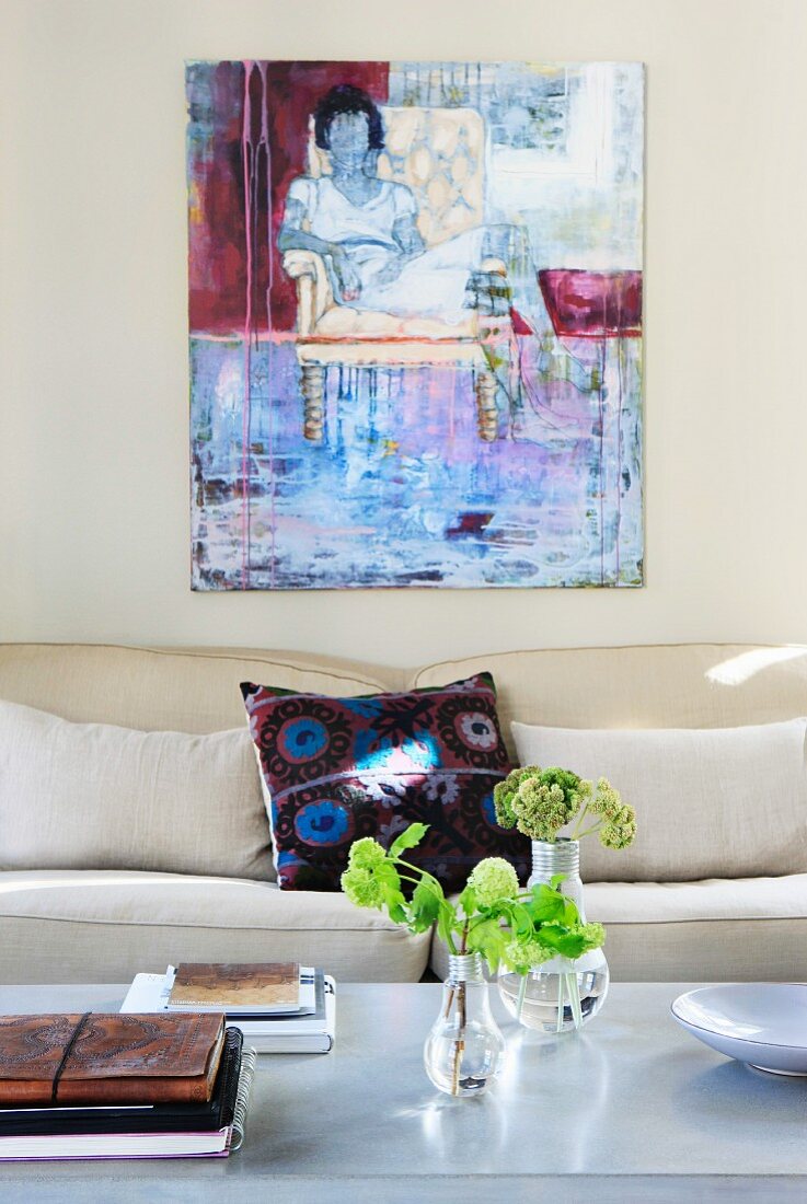 Flowers on coffee table in front of modern sofa and painting on pale grey wall