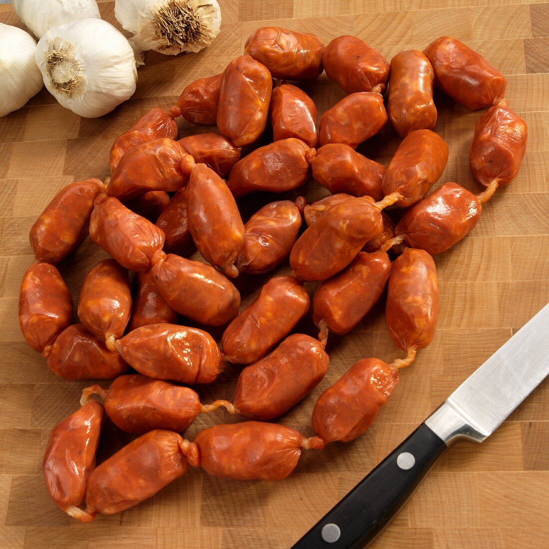 Spanish Spicy Small Link Sausages on a Cutting Board; Knife