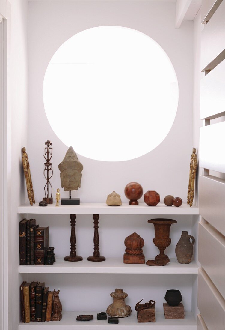 Collection of old books and sculptures on white shelves