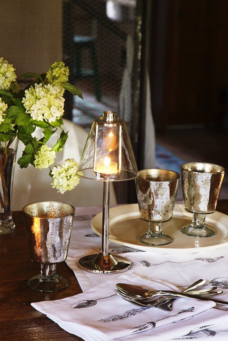 Elegantes Windlicht mit Fuss neben Vintage Weingläsern auf Tisch