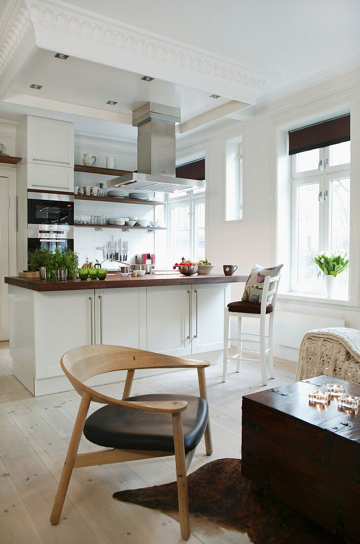 Interior with modern wooden chair next to trunk-like coffee table and open kitchen with central island