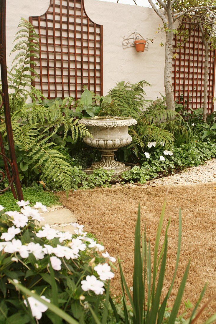 Antique, Greek urn surrounded by ferns and trellising on stone wall of courtyard