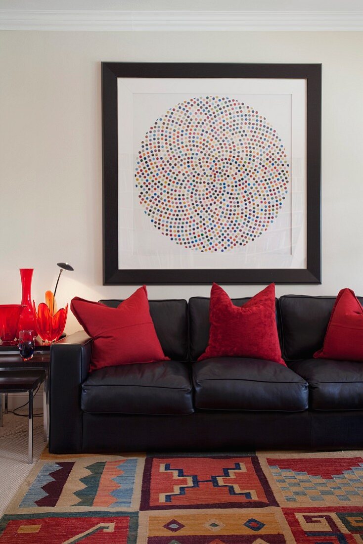 Black leather sofa with red, decorative pillows under an abstract painting