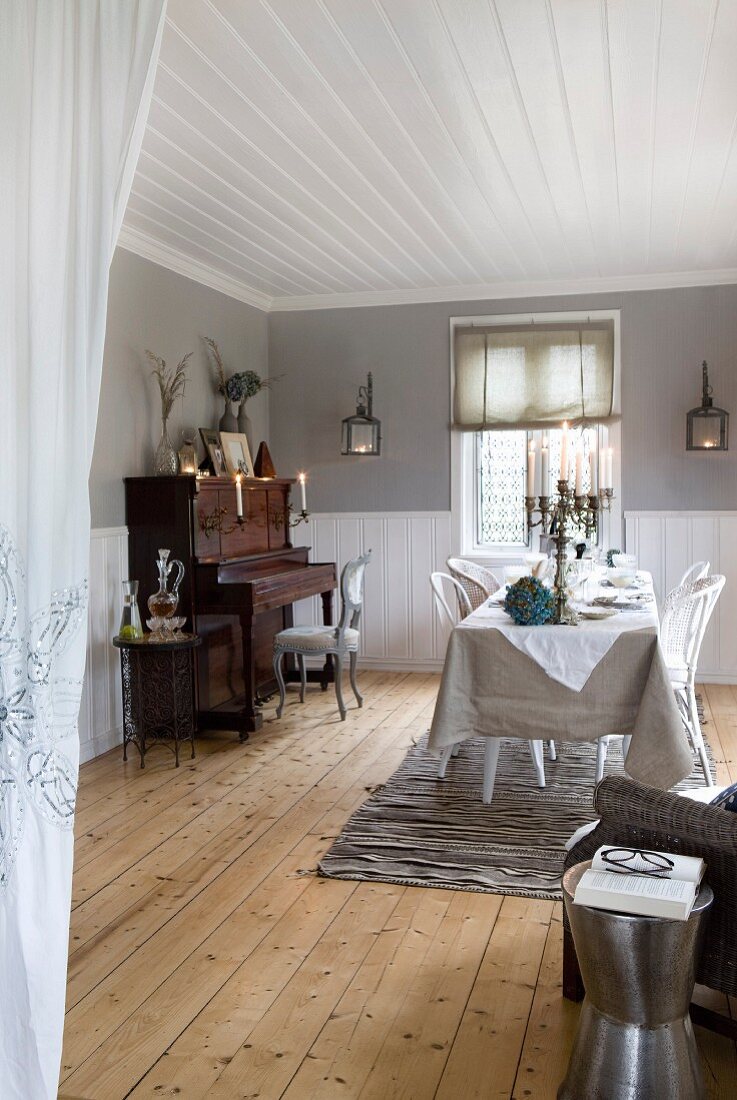 Set table opposite piano in spacious dining room with rustic wooden floor and white wooden ceiling