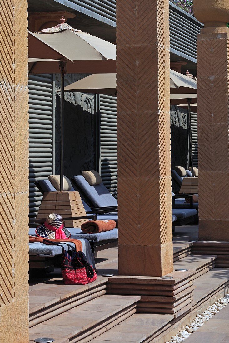 Sun loungers and parasols behind masonry columns on terrace of art deco hotel