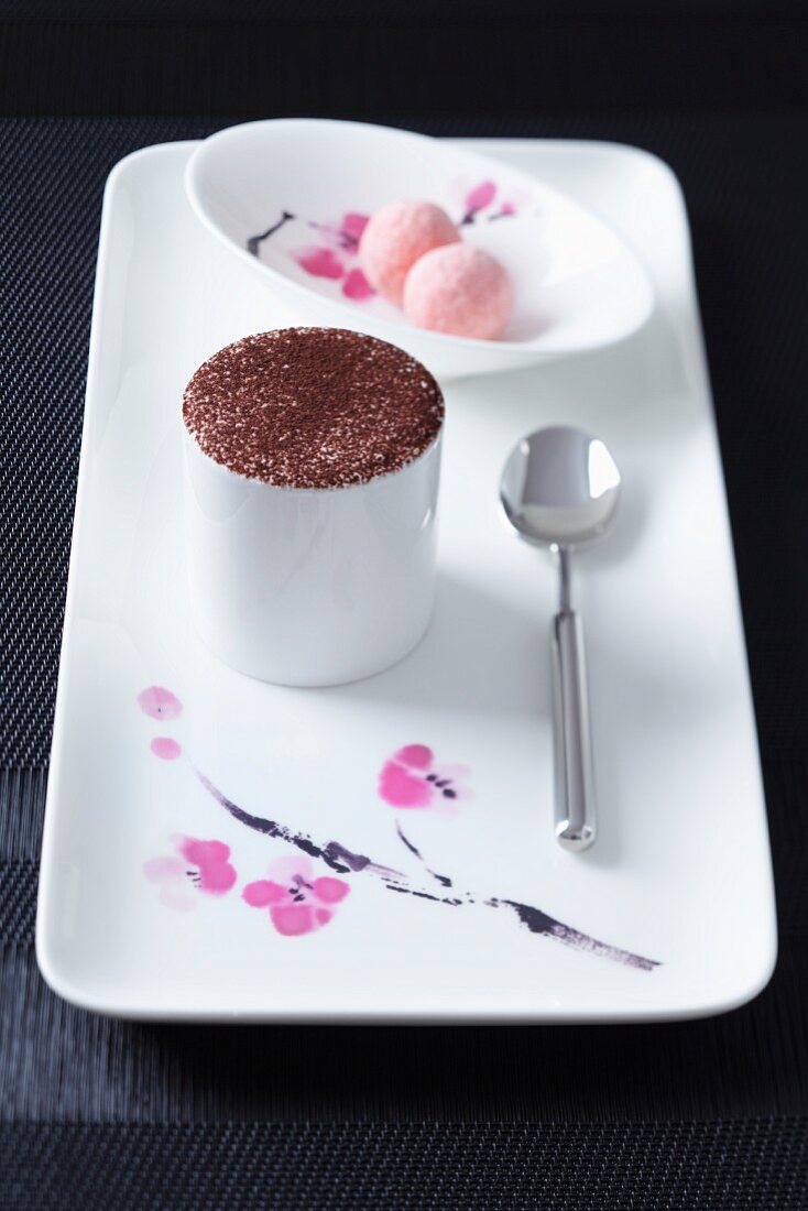 A porcelain platter with tiramisu in a cup and a dish of pralines