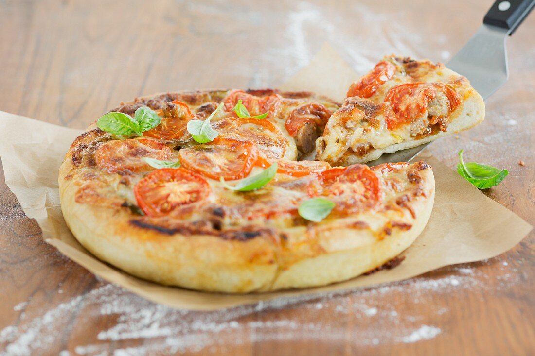 A deep dish pizza with basil leaves (Chicago, USA); one slice is on a pizza shovel