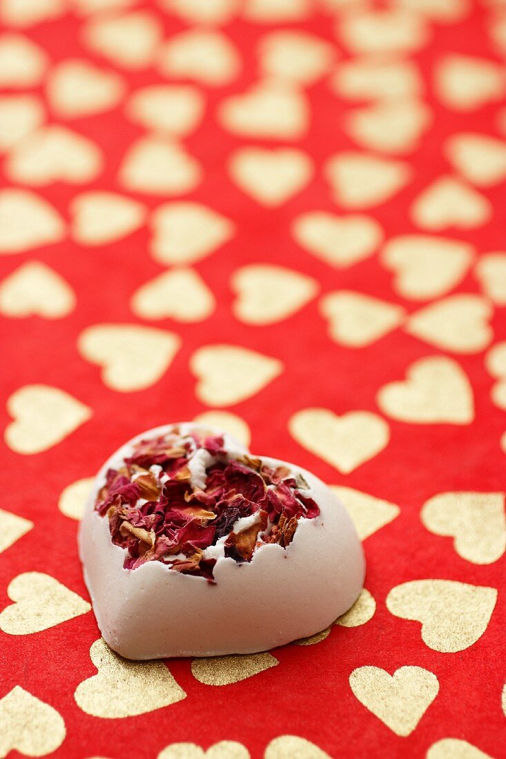 Bath bomb with rose petals on a red background patterned with hearts