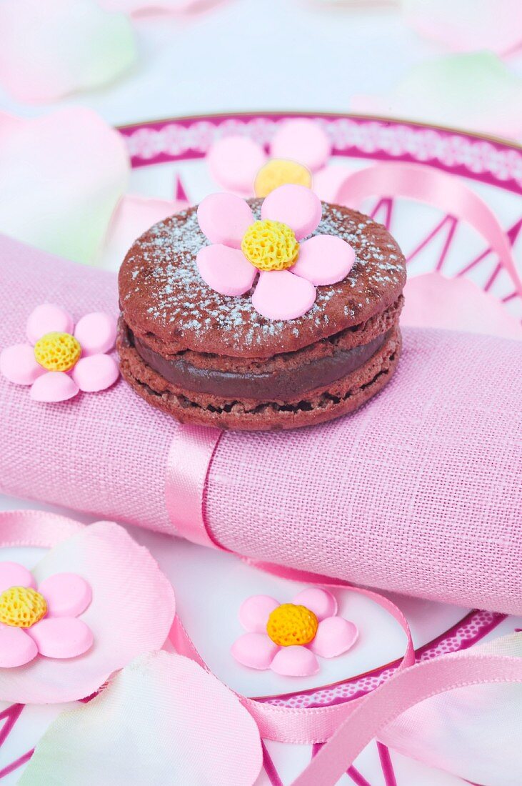 Schokoladen-Macaron mit Zuckerblüten auf rosa Stoffserviette