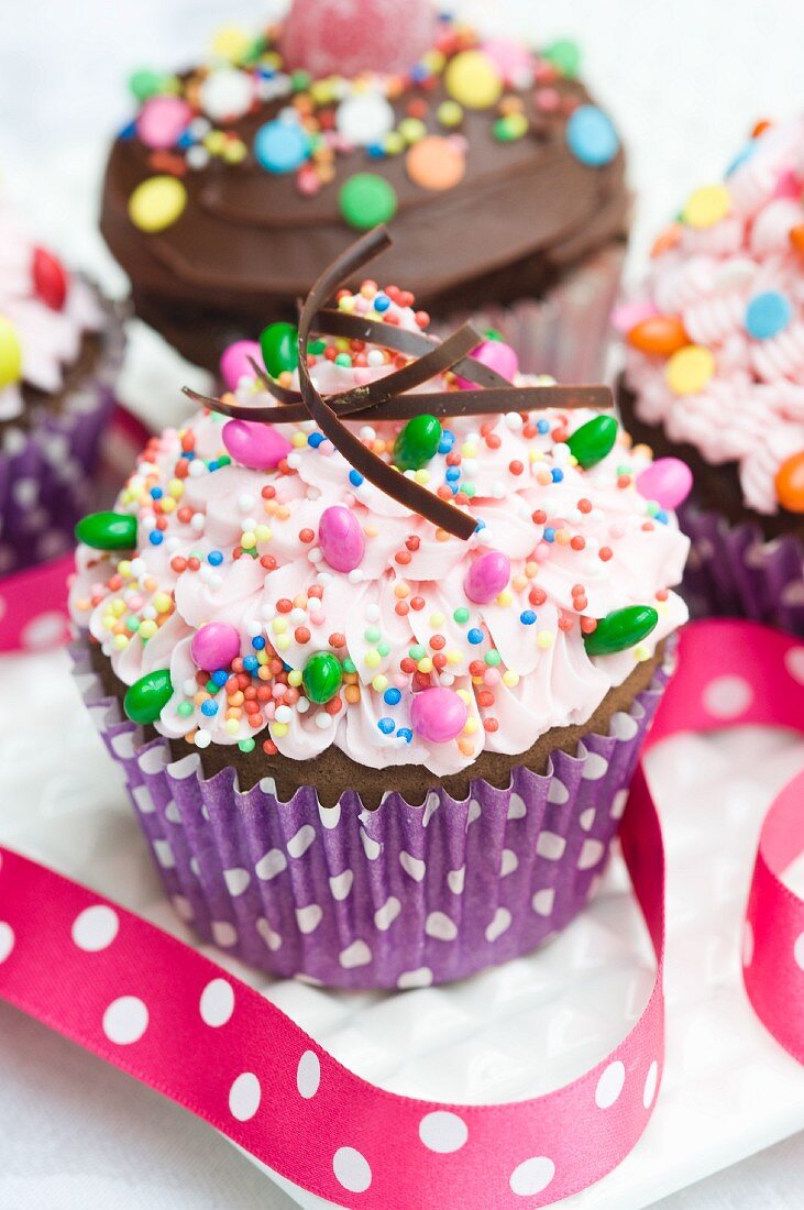 Two cupcakes topped with pink buttercream icing, chocolate icing and sweets