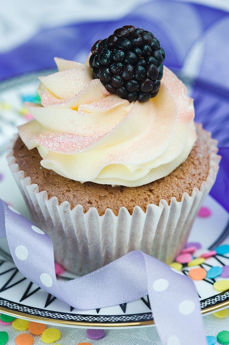 A vanilla cupcake with cream and a fresh blackberry