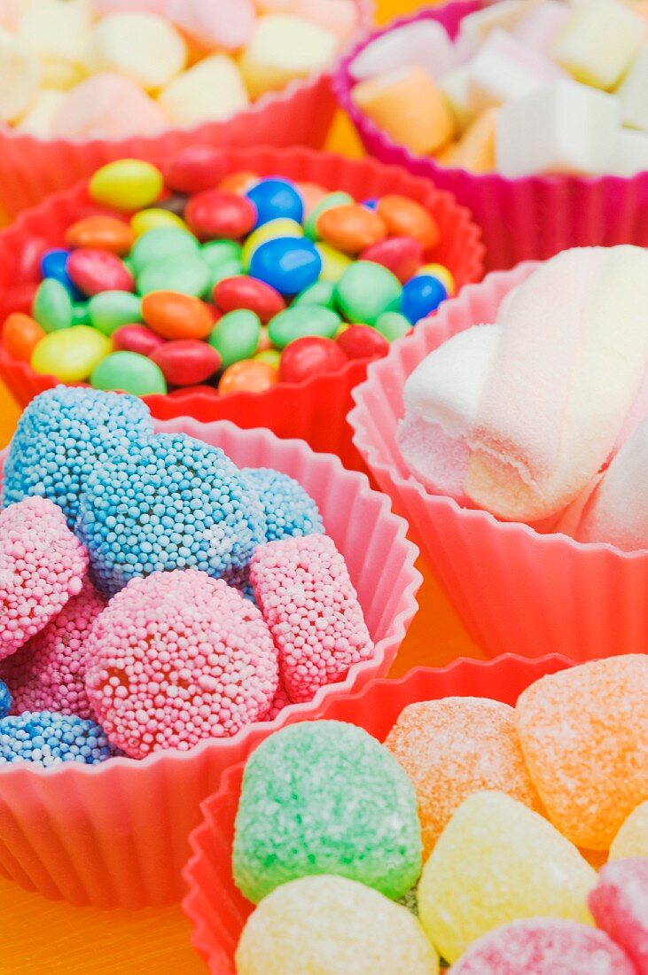 An assortment of sweets: jelly sweets, chocolate beans and marshmallows in colourful plastic bowls