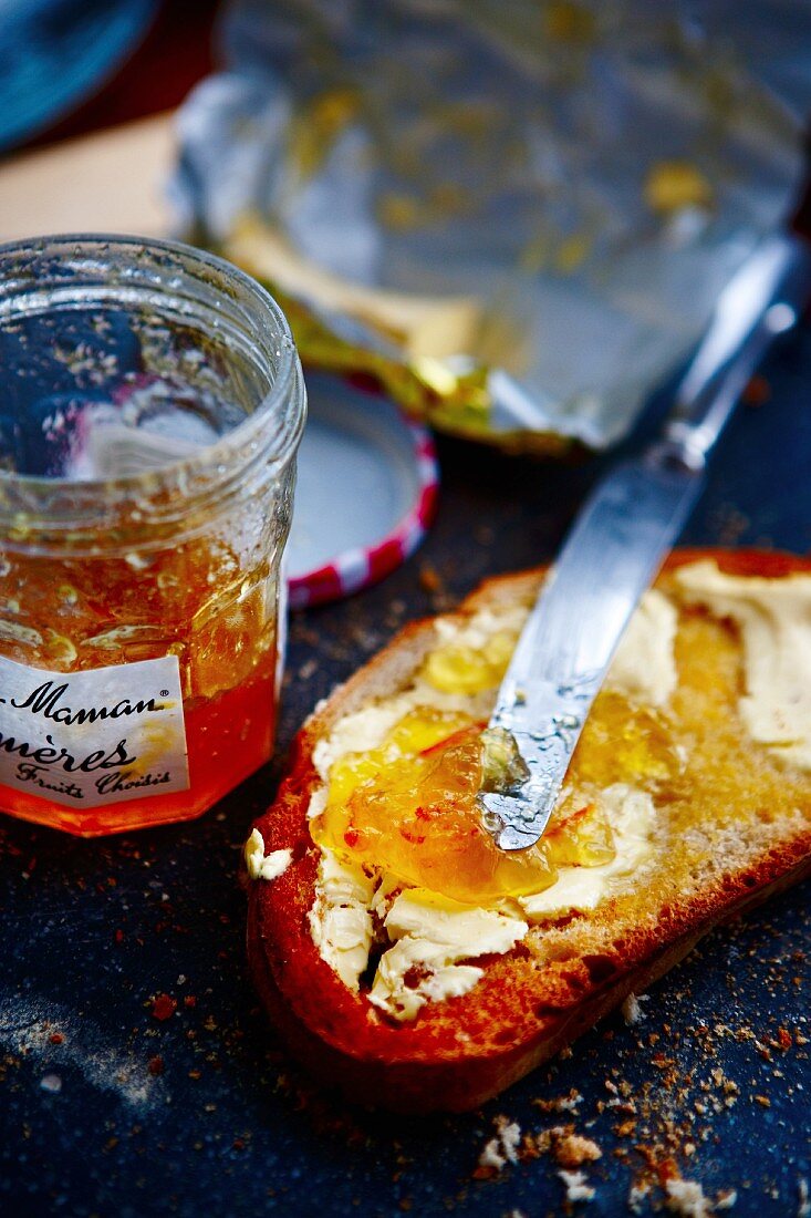 A slice of bread with butter and marmalade, a jar of marmalade and a butter wrapper