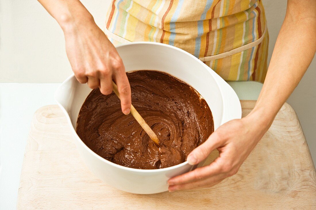 A woman stirs chocolate cake mixture with a wooden spoon in a bowl