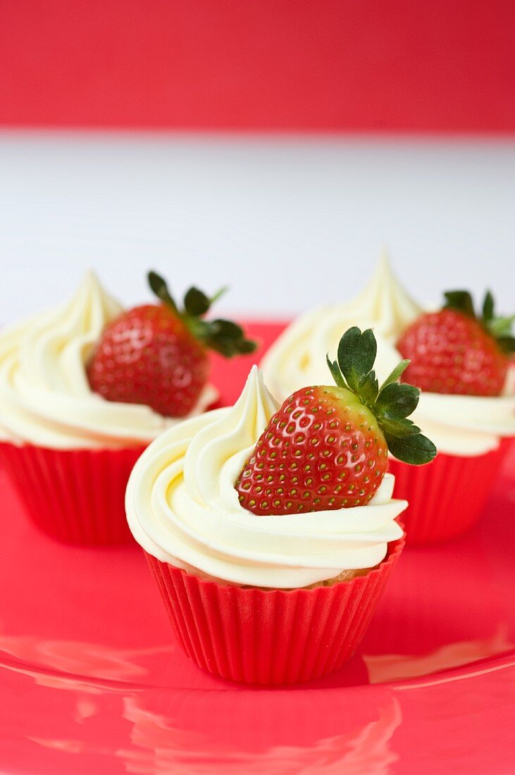 Three cupcakes with vanilla icing and fresh strawberries