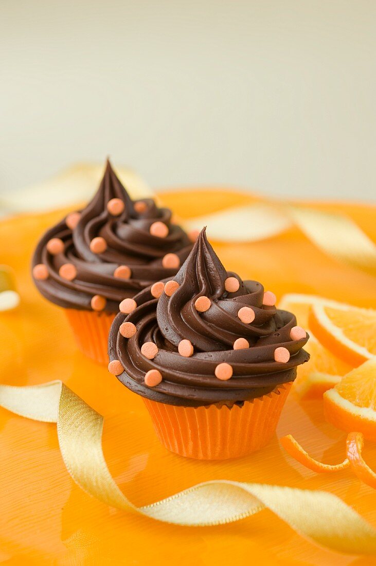 Zwei Schokoladencupcakes mit Zuckerkonfetti und Orangen