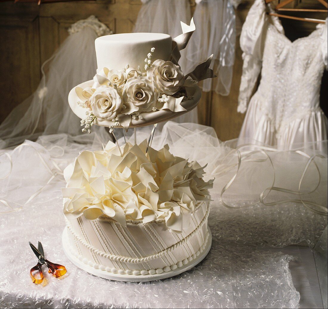 Hochzeitstorte mit weißem Hut und Brautkleid im Hintergrund
