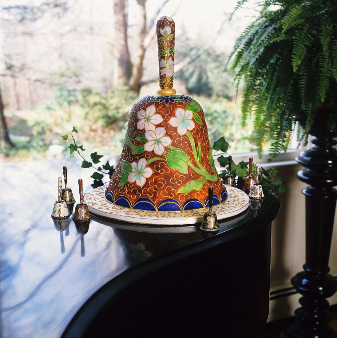 Hochzeitstorte in Glockenform auf Klavier, umgeben von Hochzeitsglocken