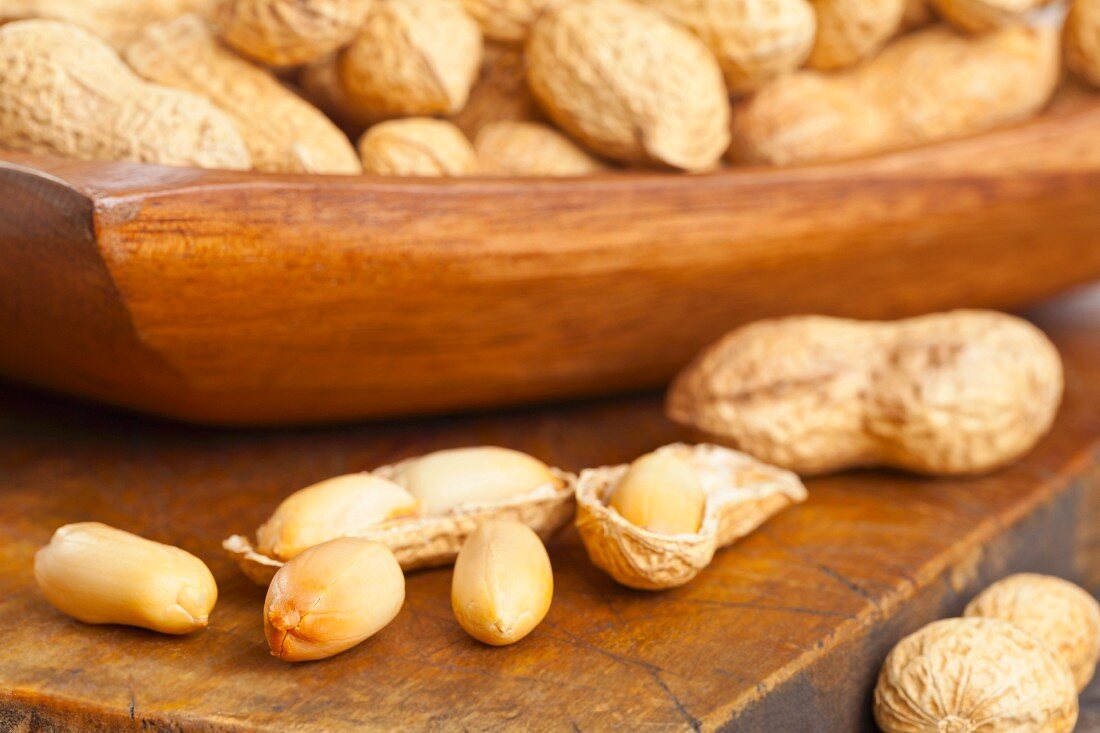 Peanuts, whole and shelled, in and in front of a wooden bowl