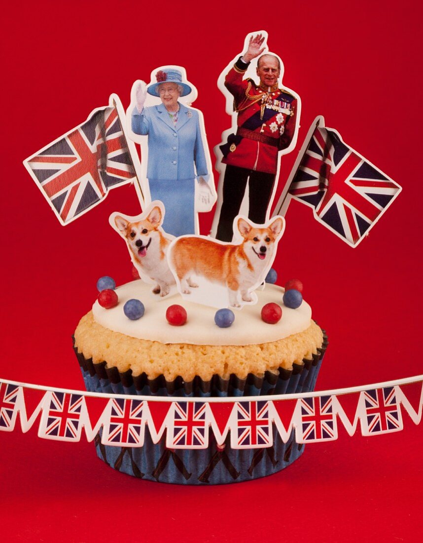 A cupcake topped with Queen Elizabeth II of England and Prince Philip, Corgis and Union Jack flags