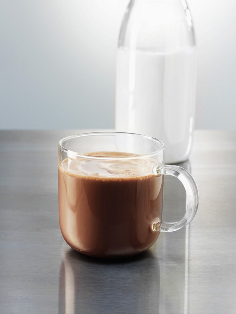 A glass cup of hot cocoa next to a bottle of milk
