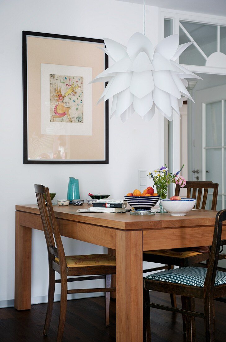 Modern dining table and traditional chairs below Bauhaus pendant lamp with fish scale shade in front of framed picture on wall