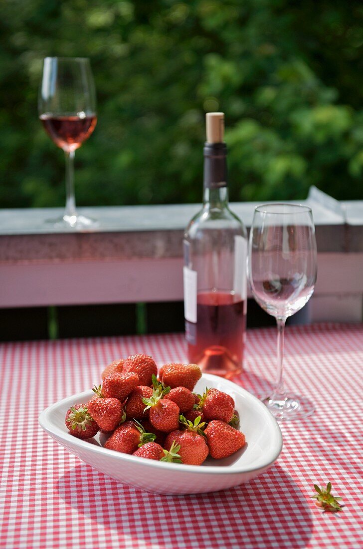 Eine Schale Erdbeeren und Rosewein auf dem Balkontisch mit karierter Tischdecke