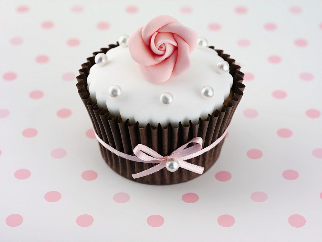 A cupcake decorated with a sugar rose and silver balls
