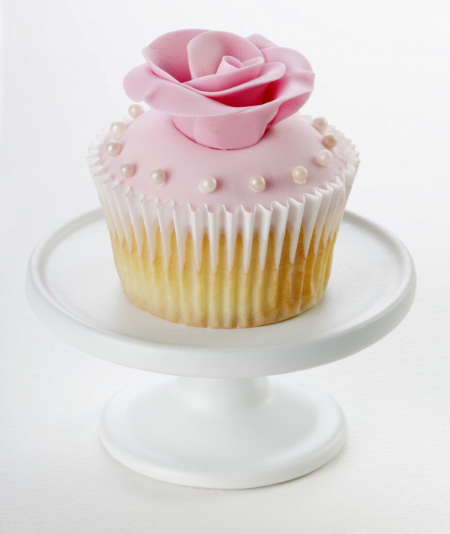 A cupcake with pink glaze, a sugar rose and small sugar pearls