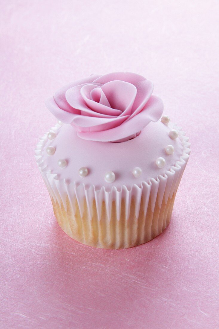 A cupcake with pink glaze, a sugar rose and sugar pearls